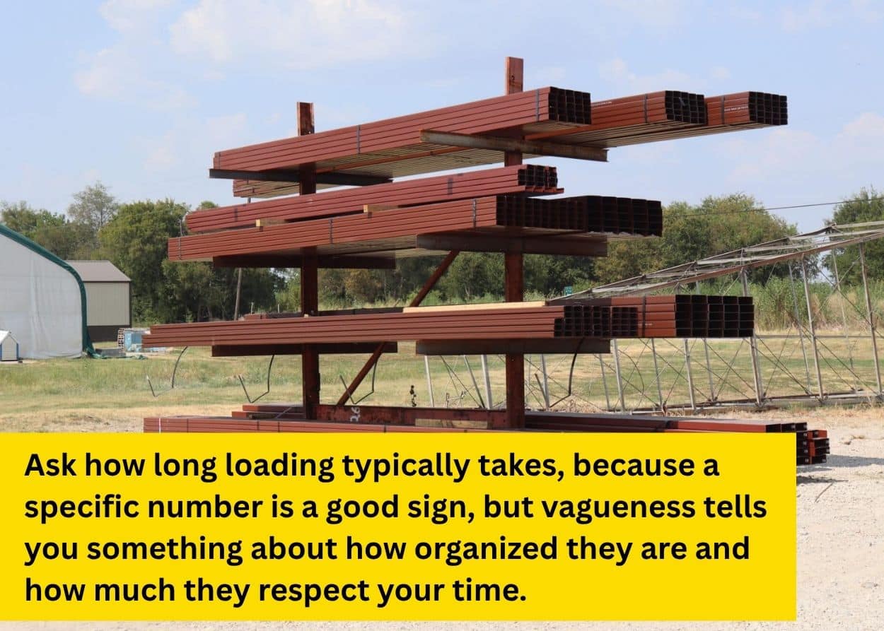Bundles of red metal building materials stacked on an outdoor storage rack for loading and pickup